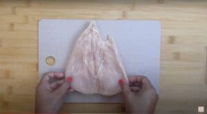 Person holding butterflied chicken breast on cutting board, ready for cooking preparation.